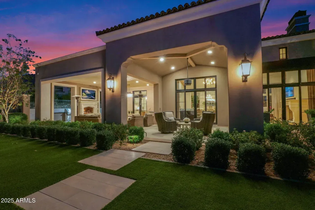 Exterior of a modern home at dusk with a covered patio, manicured lawn, and colorful sky.