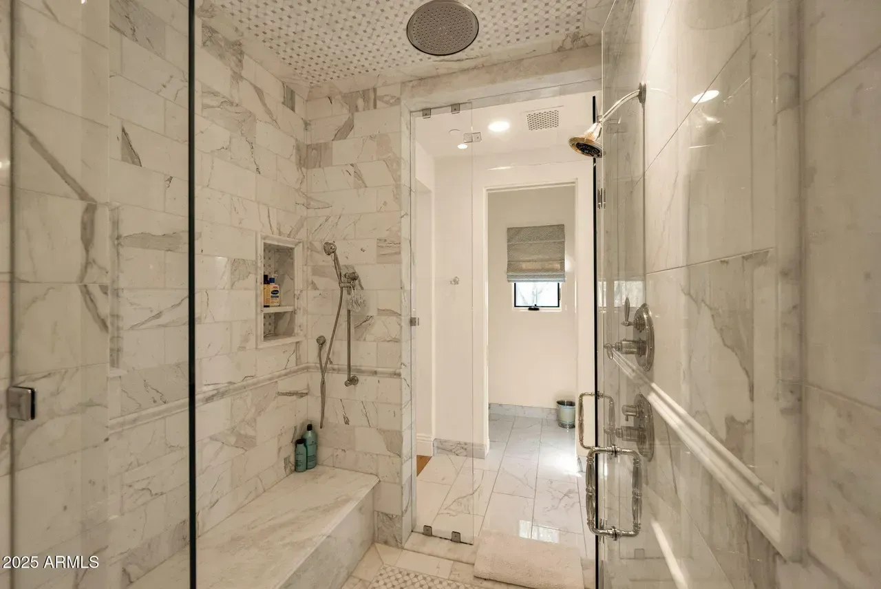 Marble-tiled bathroom with a glass shower door. A bench is in the shower.