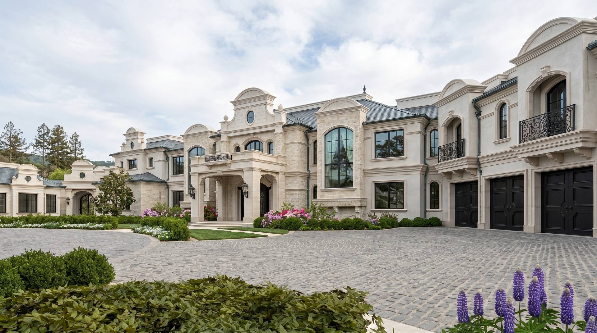 French luxury mansion with ornate stone facade, arched windows, garage doors, and a landscaped gravel courtyard.
