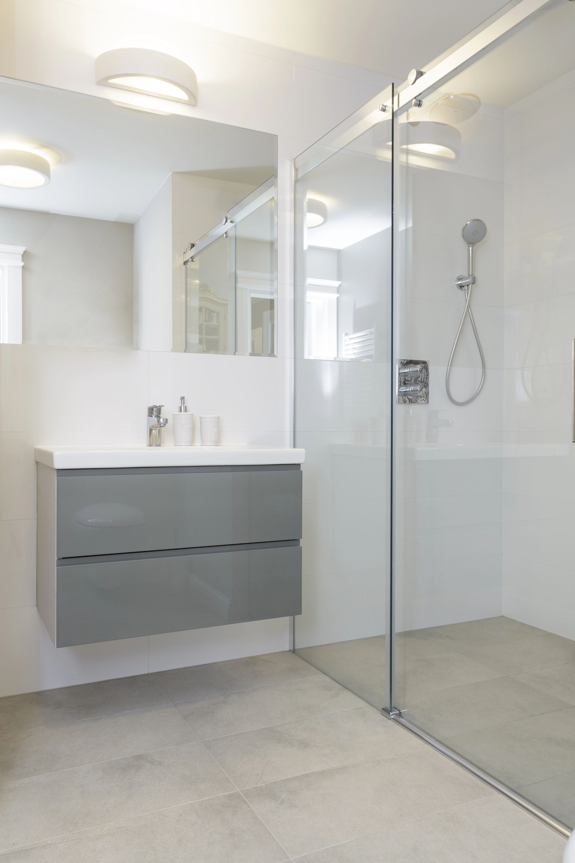 Baño moderno blanco con ducha de cristal, espejo de tocador y mueble de lavabo flotante gris.