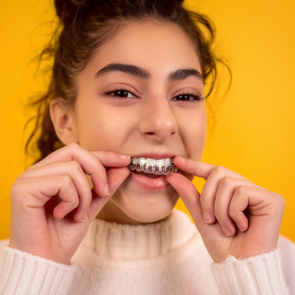 Smiling person holding metal braces against teeth against a bright yellow background
