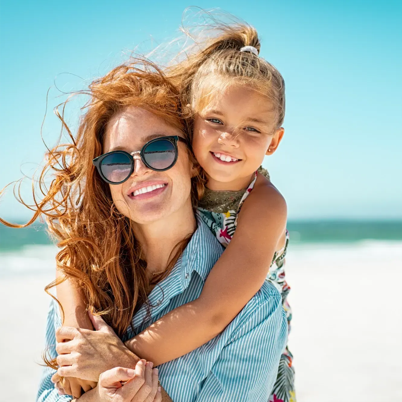 Woman with sunglasses being hugged by her daughter on the beach