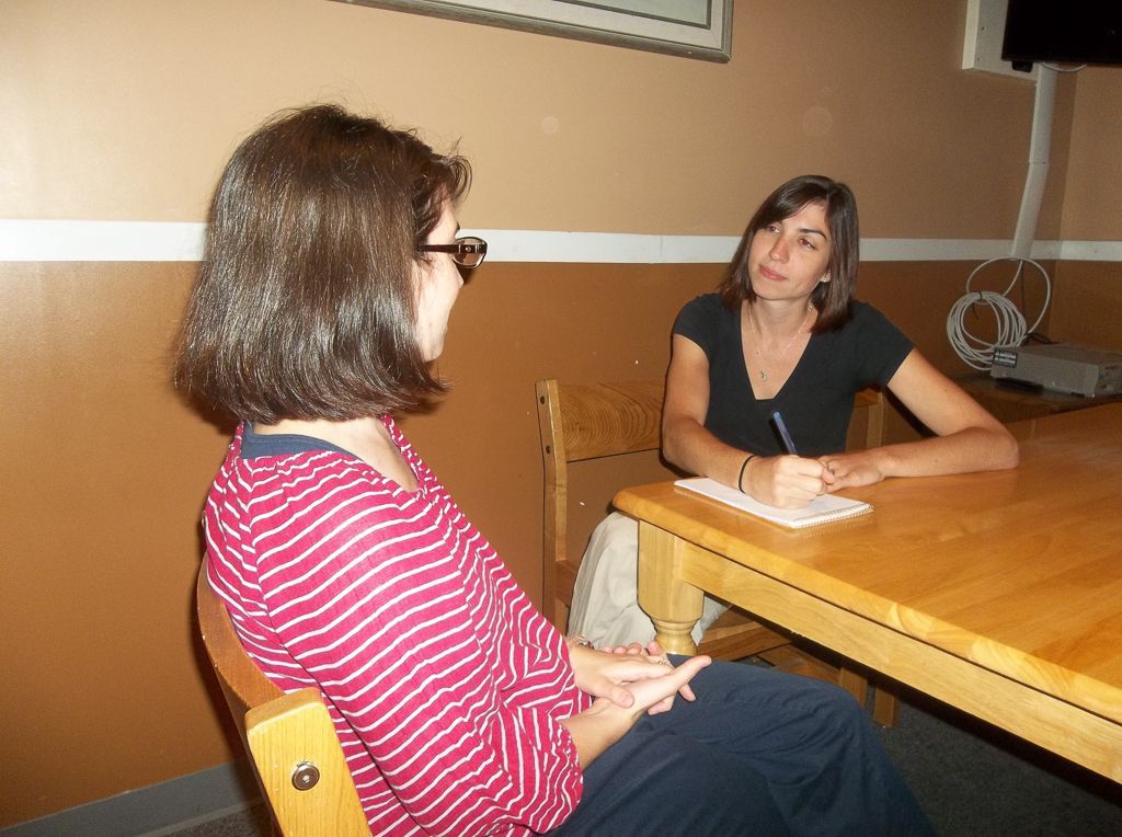 Two women are sitting at a table and one is writing on a piece of paper