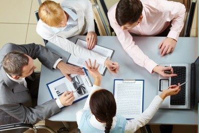 A group of people are sitting around a table with papers and a laptop.