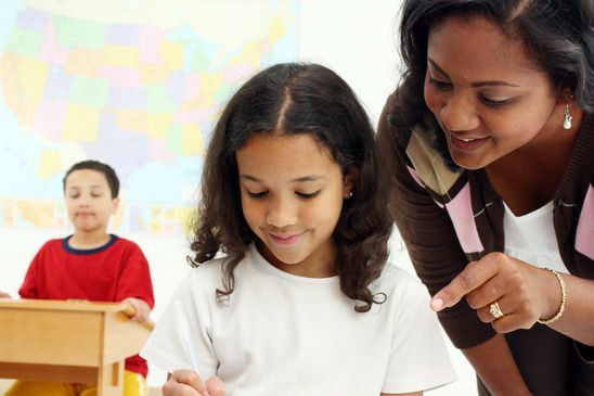 A woman is helping a young girl with her homework in a classroom