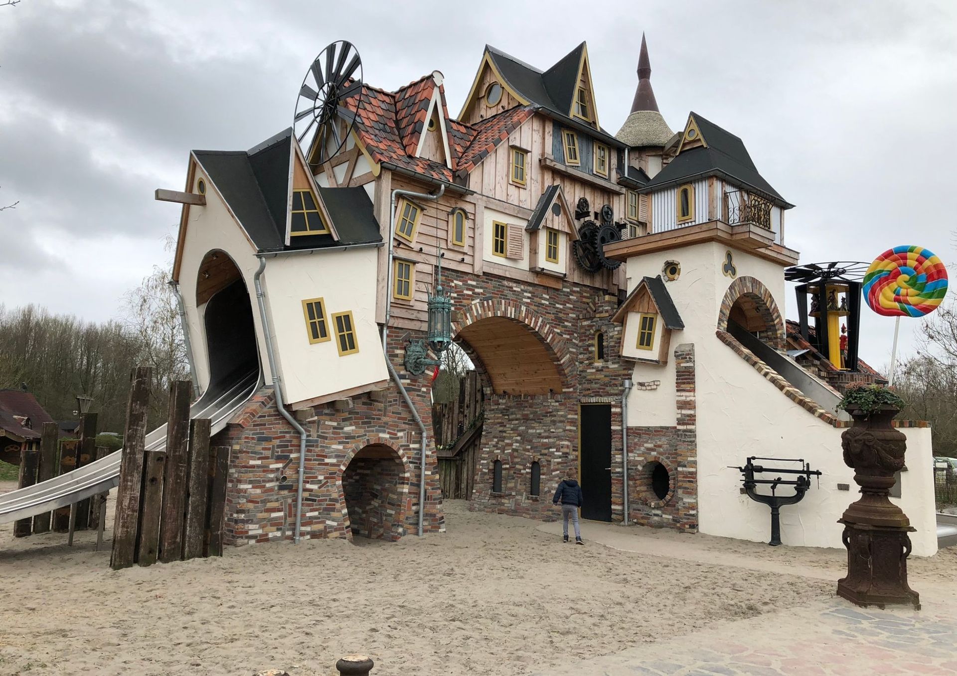 Een speelse speeltuin met boogvormige ingangen, een windmolen en glijbanen, op een zandondergrond.
