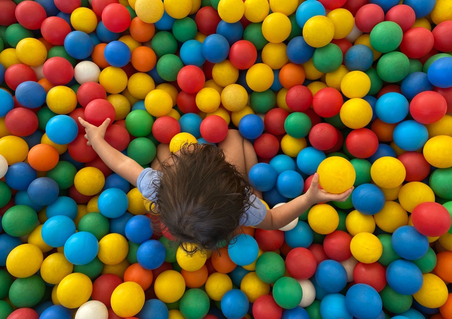 Kind in een kleurrijke ballenbak dat naar een gele bal reikt.