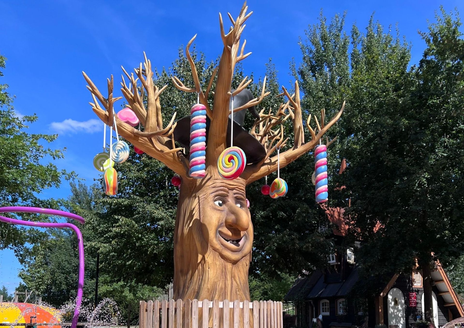 Een speelse boomsculptuur met een gezicht, versierd met snoep, in een parkomgeving.