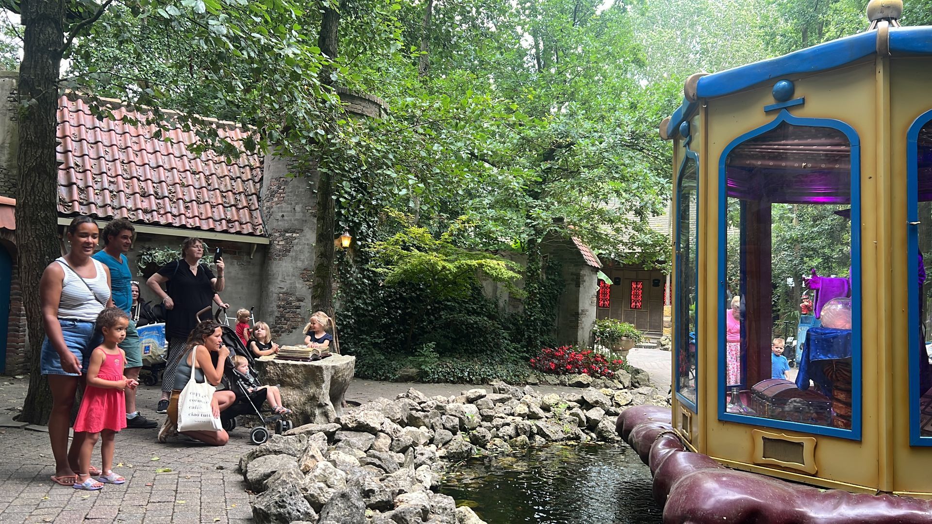 Mensen bij een vijver, een kleurrijke attractie en een gebouw met een rood pannendak.