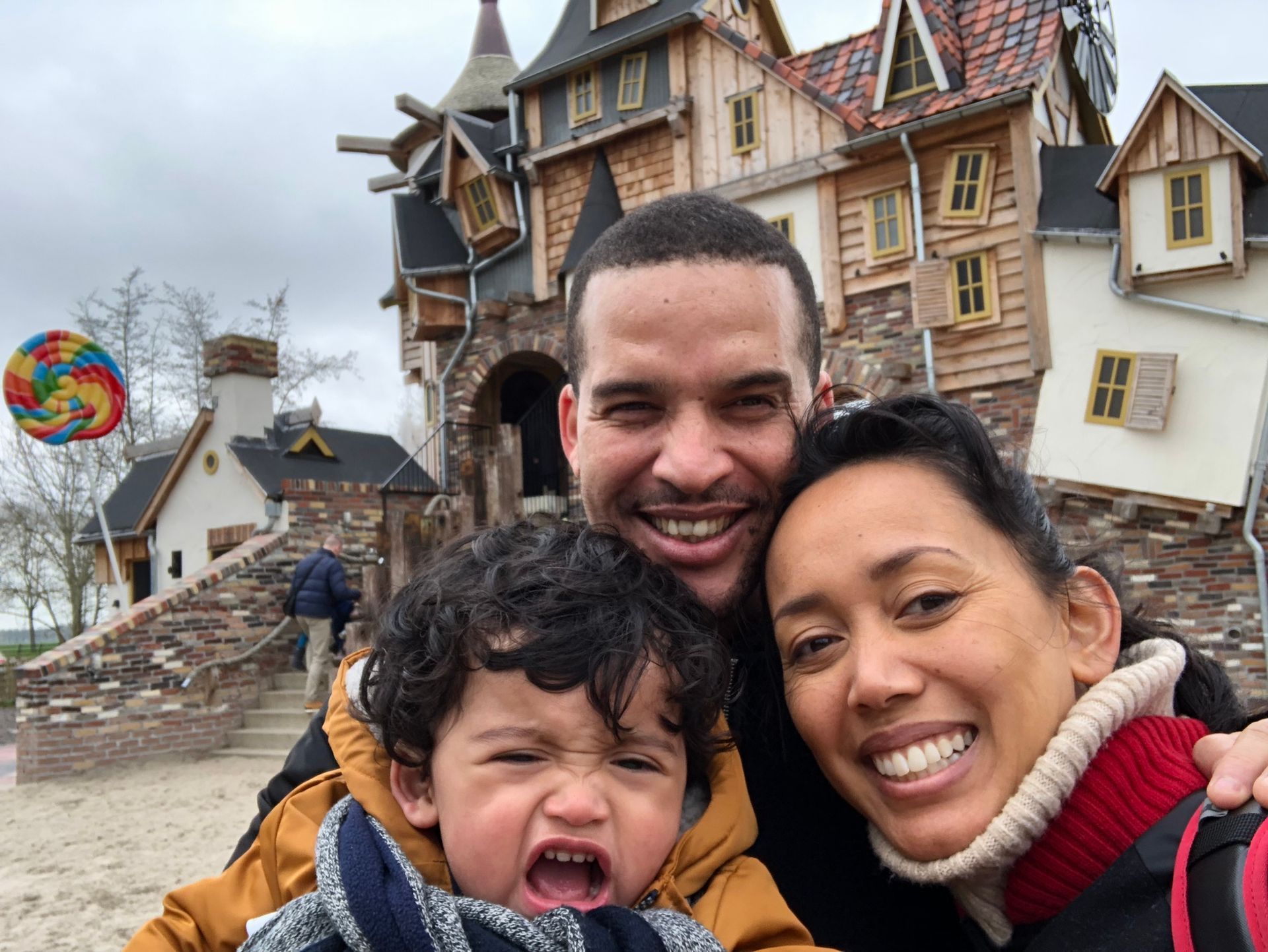 Familieselfie voor een speels gebouw, met een kind dat een gek gezicht trekt en een kleurrijke lolly.