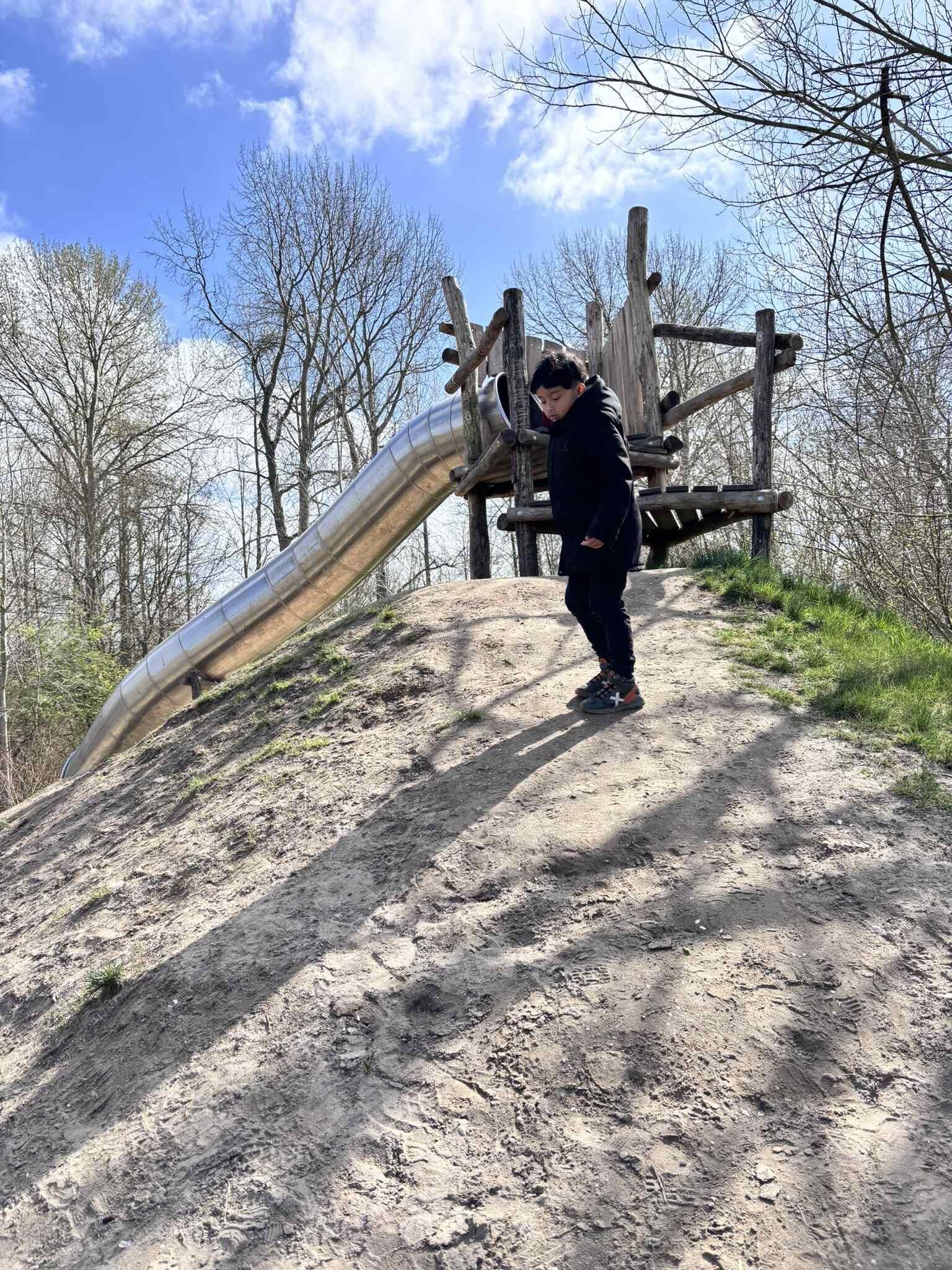 Kind staat op een zonnige dag bij een glijbaan in een speeltuin.