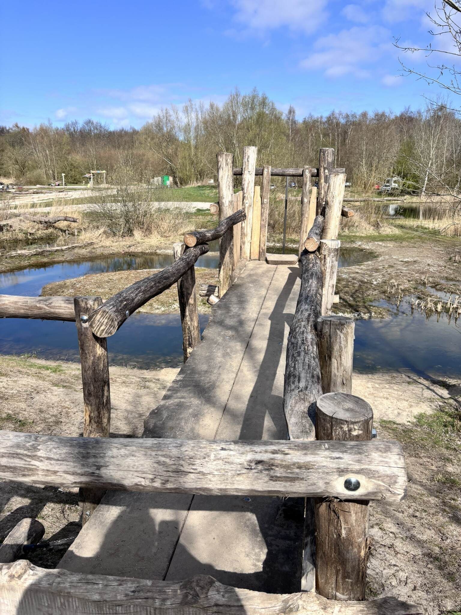 Houten brug over een ondiepe beek in een natuurlijke buitenomgeving, op een zonnige dag.