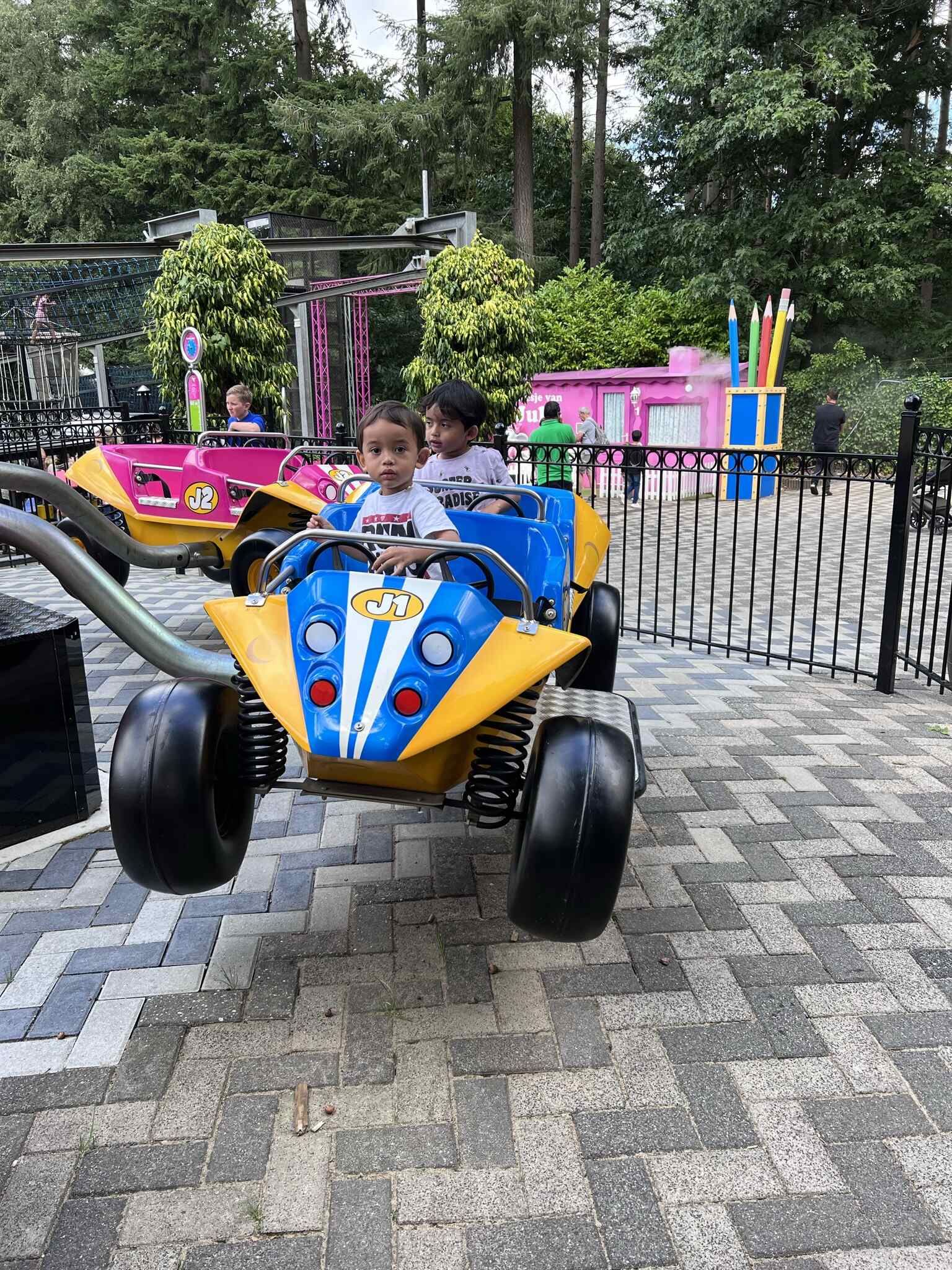 Twee kinderen in een blauw-gele, autovormige springkussen op een speeltuin.