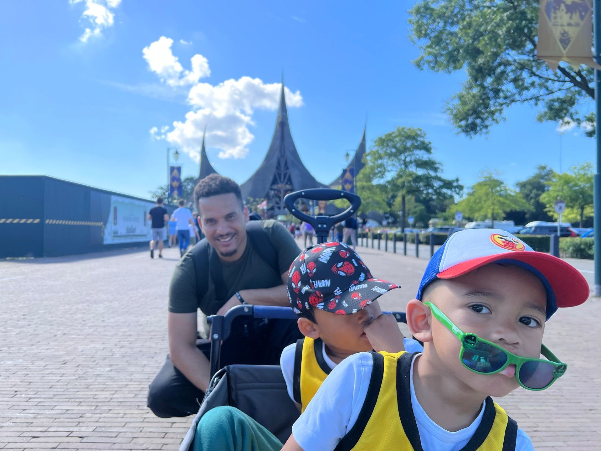 Een man met twee kinderen in een bolderwagen in een pretpark op een zonnige dag.