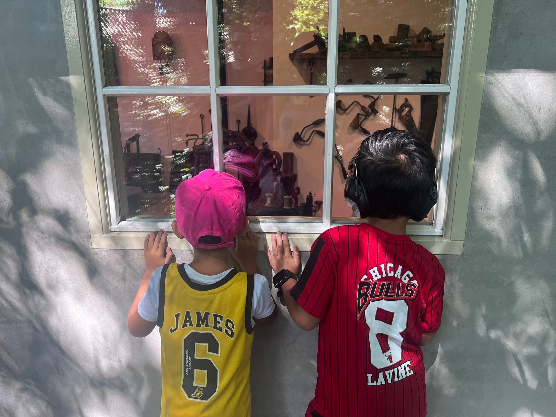 Twee kinderen kijken door een raam naar een vitrine. De ene draagt ​​een geel shirt, de andere een rood shirt.