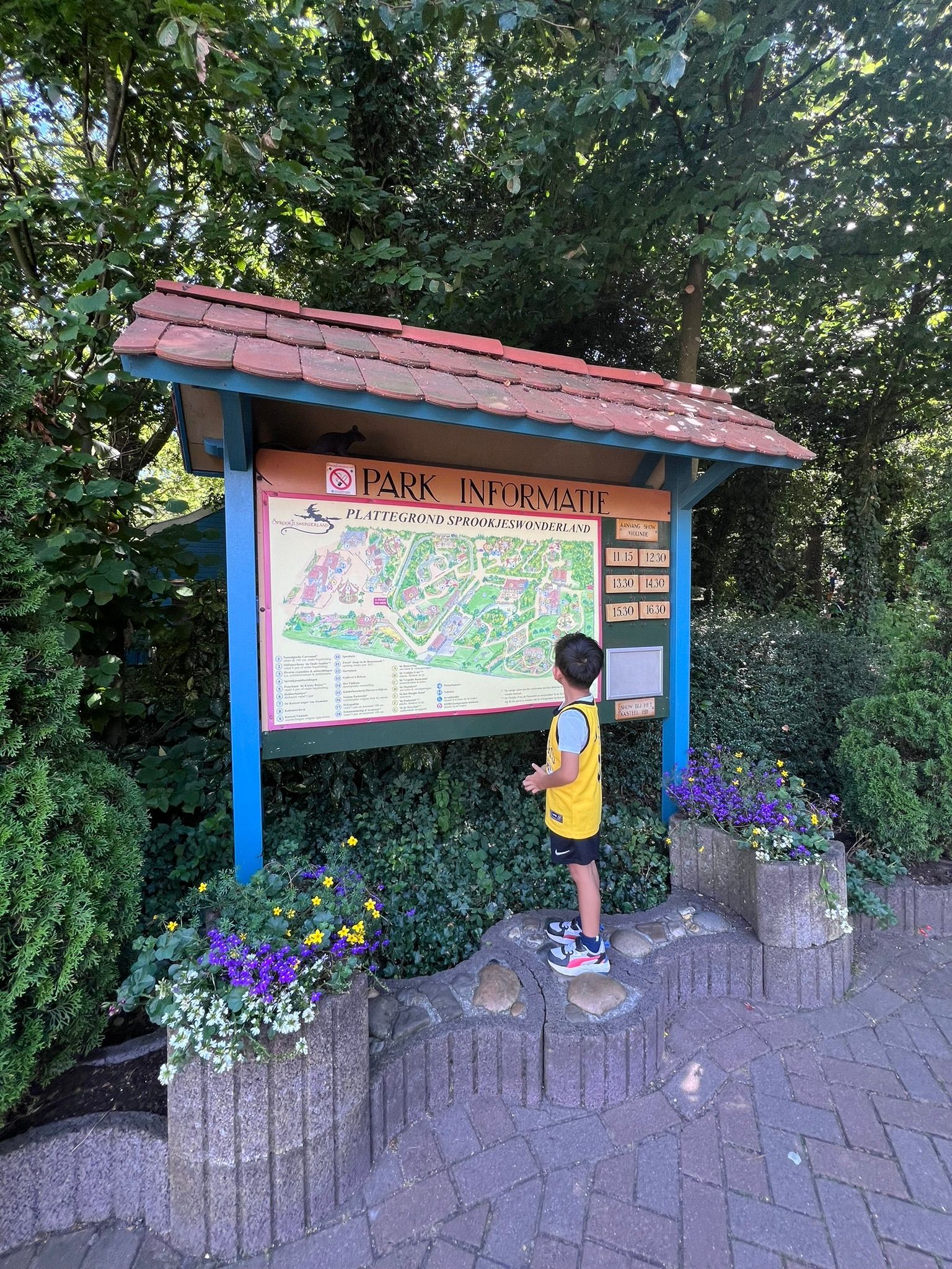 Een kind kijkt naar een kaart op een bord. Het bord staat in een park, omgeven door groen.