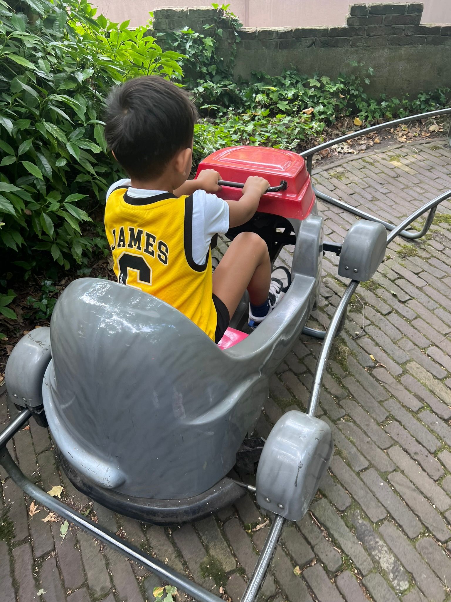 Jongen in een geel shirt, rijdend in een grijs-rode auto op een baan.