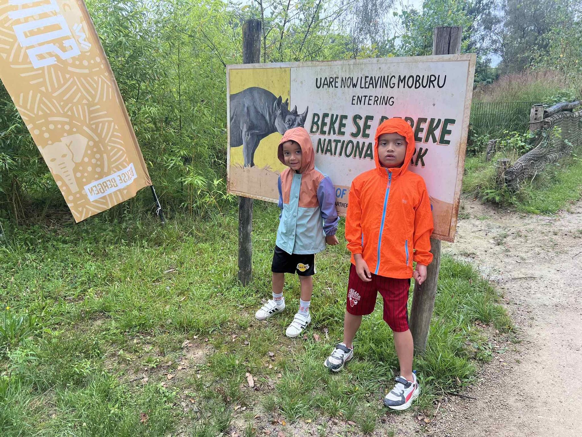 Twee kinderen in regenjassen staan bij een bord met de aanduiding Beke Sebe National Park.