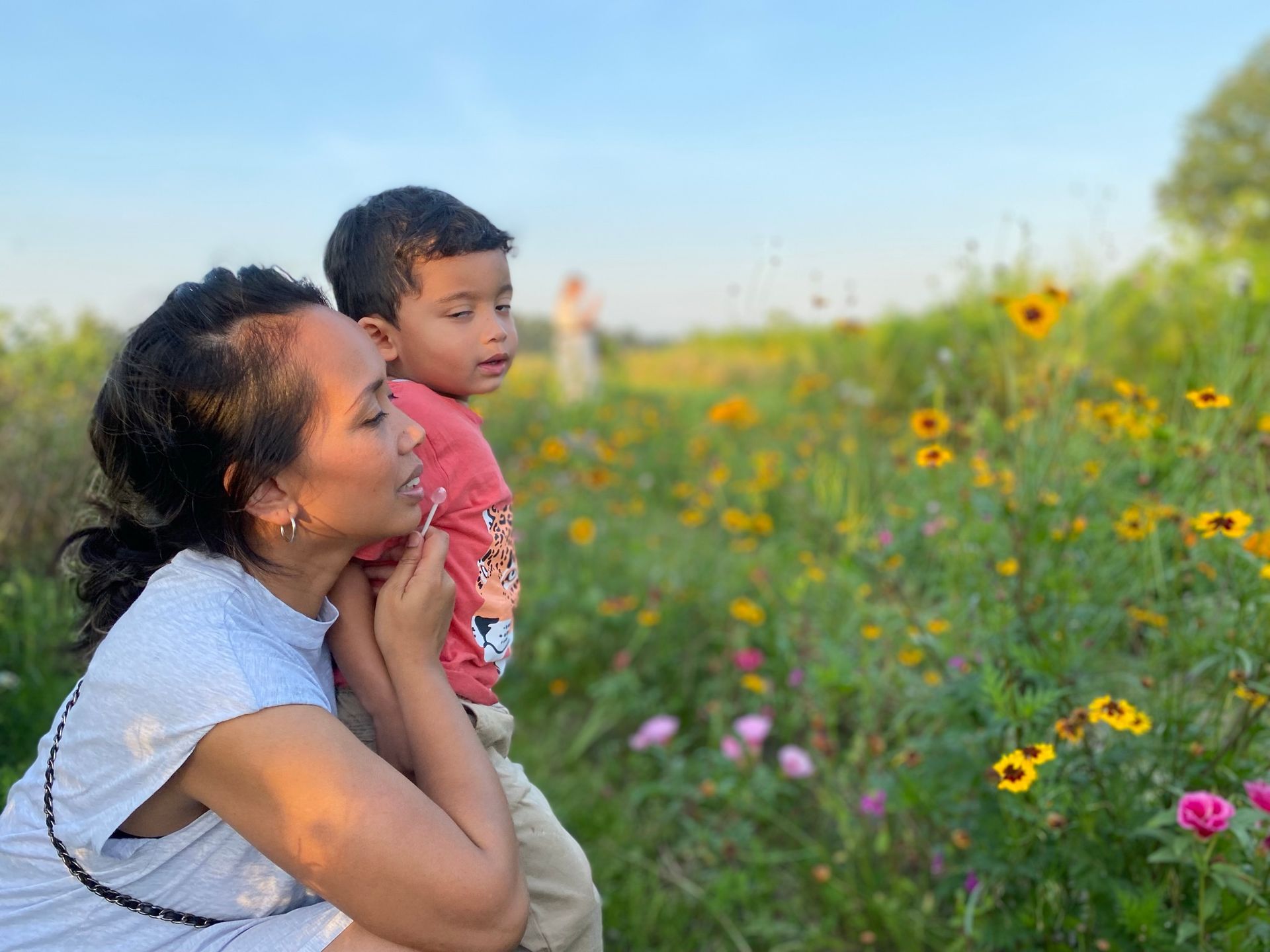 Vrouw en kind kijken naar bloemen in een veld; gouden licht.
