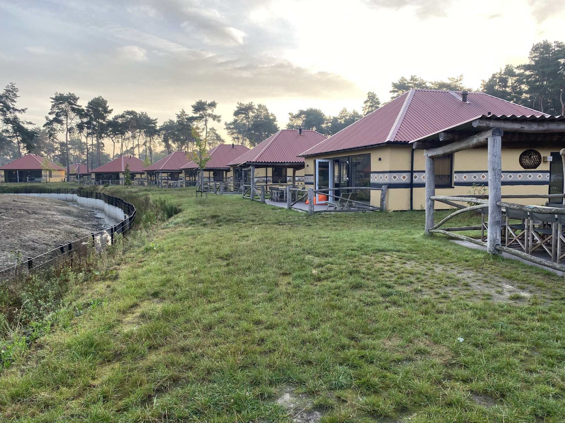 Een rij gele huisjes met rode daken op een grasveldje vlakbij bomen.