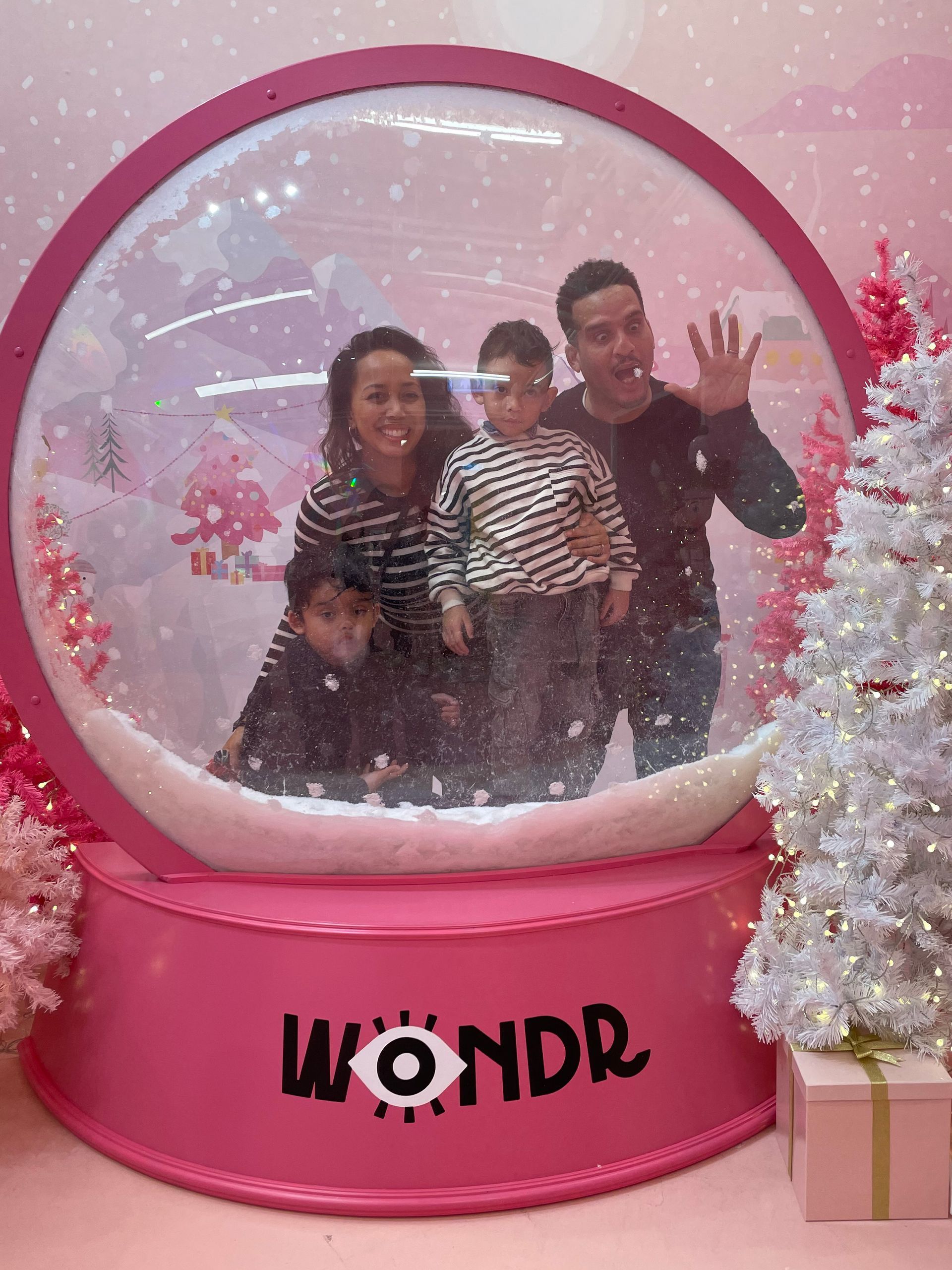 Familie poseert in een roze sneeuwbol; lachend en zwaaiend. Witte kerstboom.