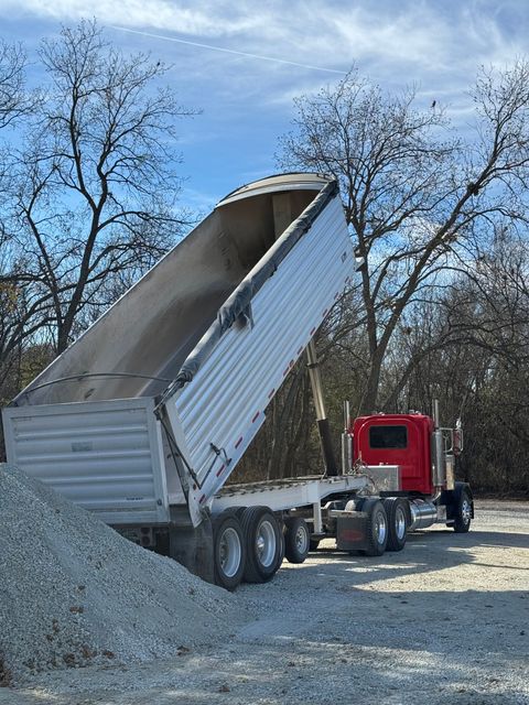 Red dump truck dumping gravel outdoors on a sunny day.