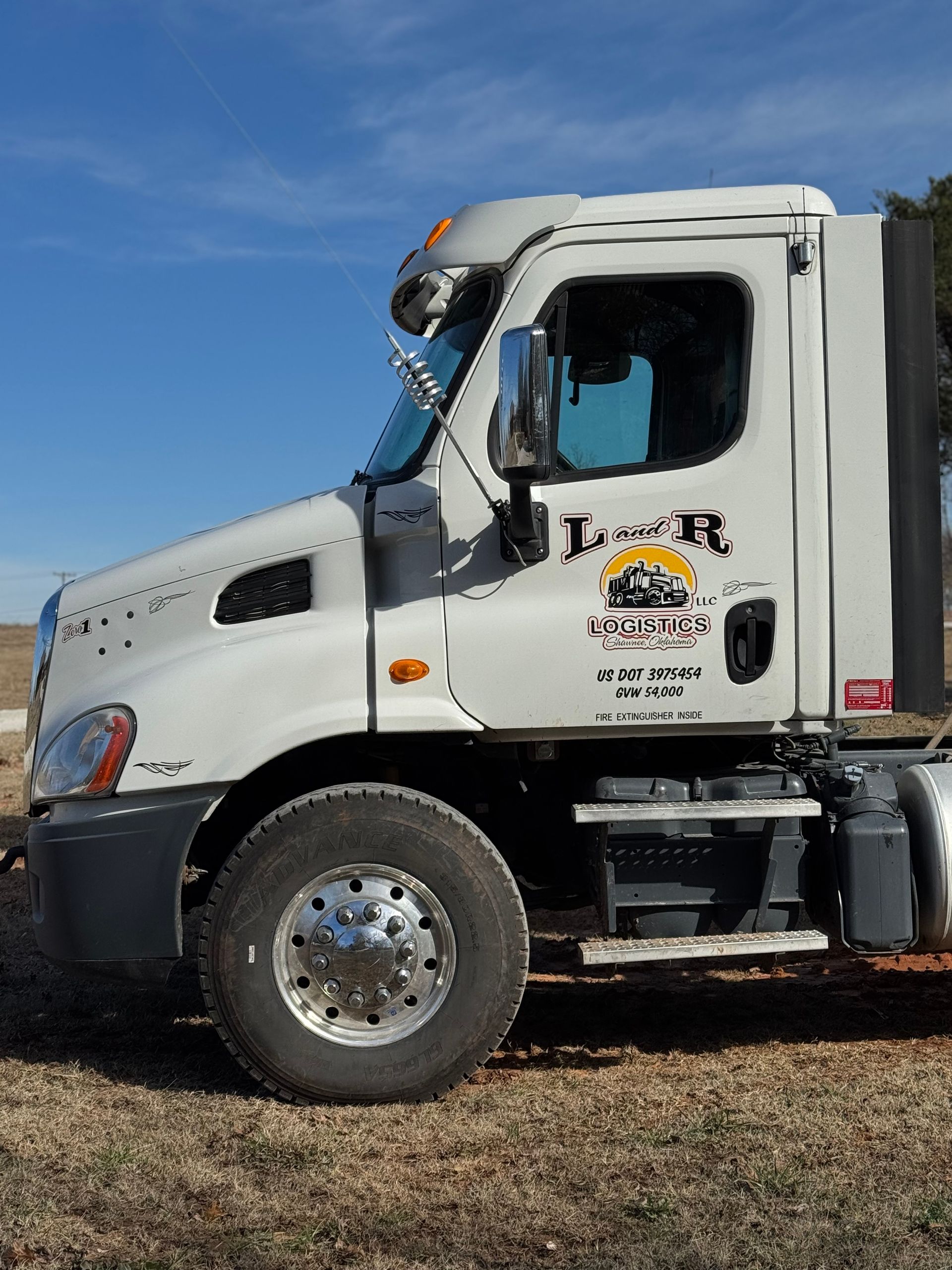 White semi-truck parked outdoors under a blue sky. The truck has the logo of 