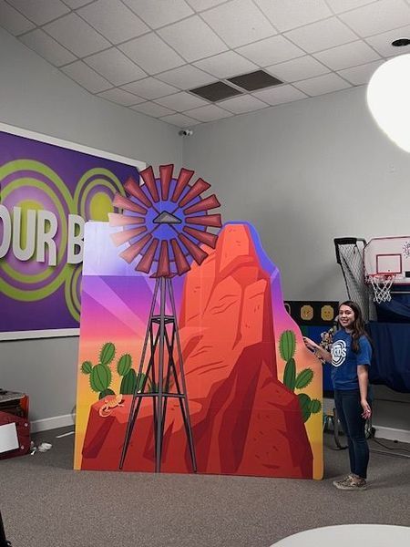 Woman next to a colorful painted desert scene with a windmill, rock formations, and cacti inside a room.