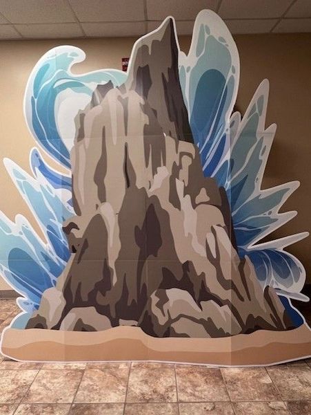 Cardboard cutout of a rock formation with ocean waves in a room.