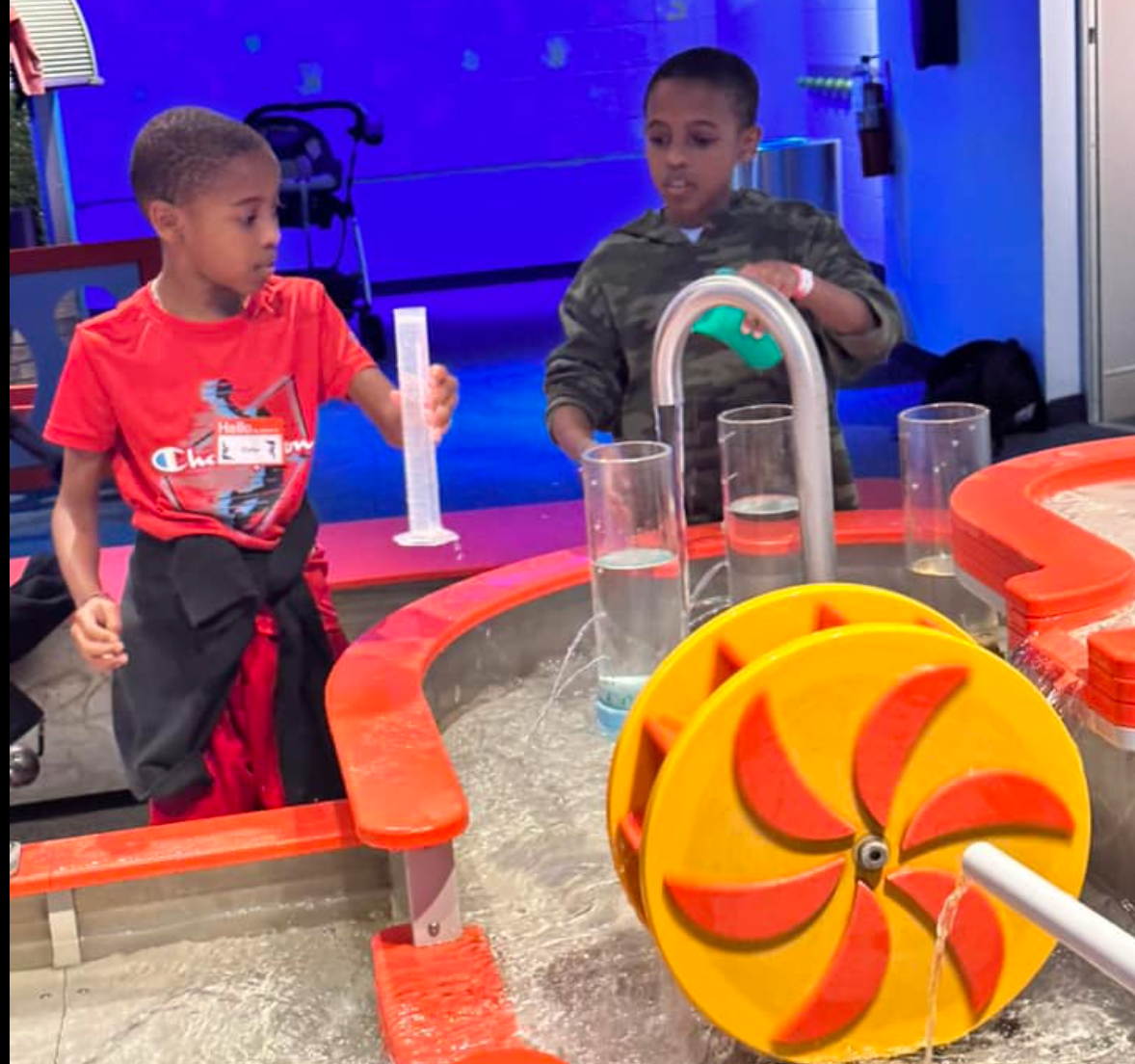 A boy in a red shirt is playing with a water wheel