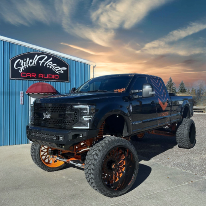 A black truck is parked in front of a building that says car audio