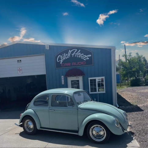 A car is parked in front of a building that says stitch house car audio