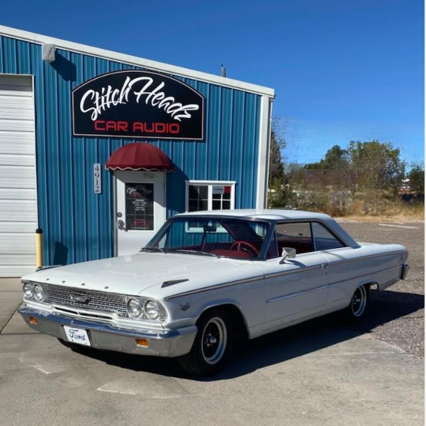 A white car is parked in front of a store called glitch hearts car audio