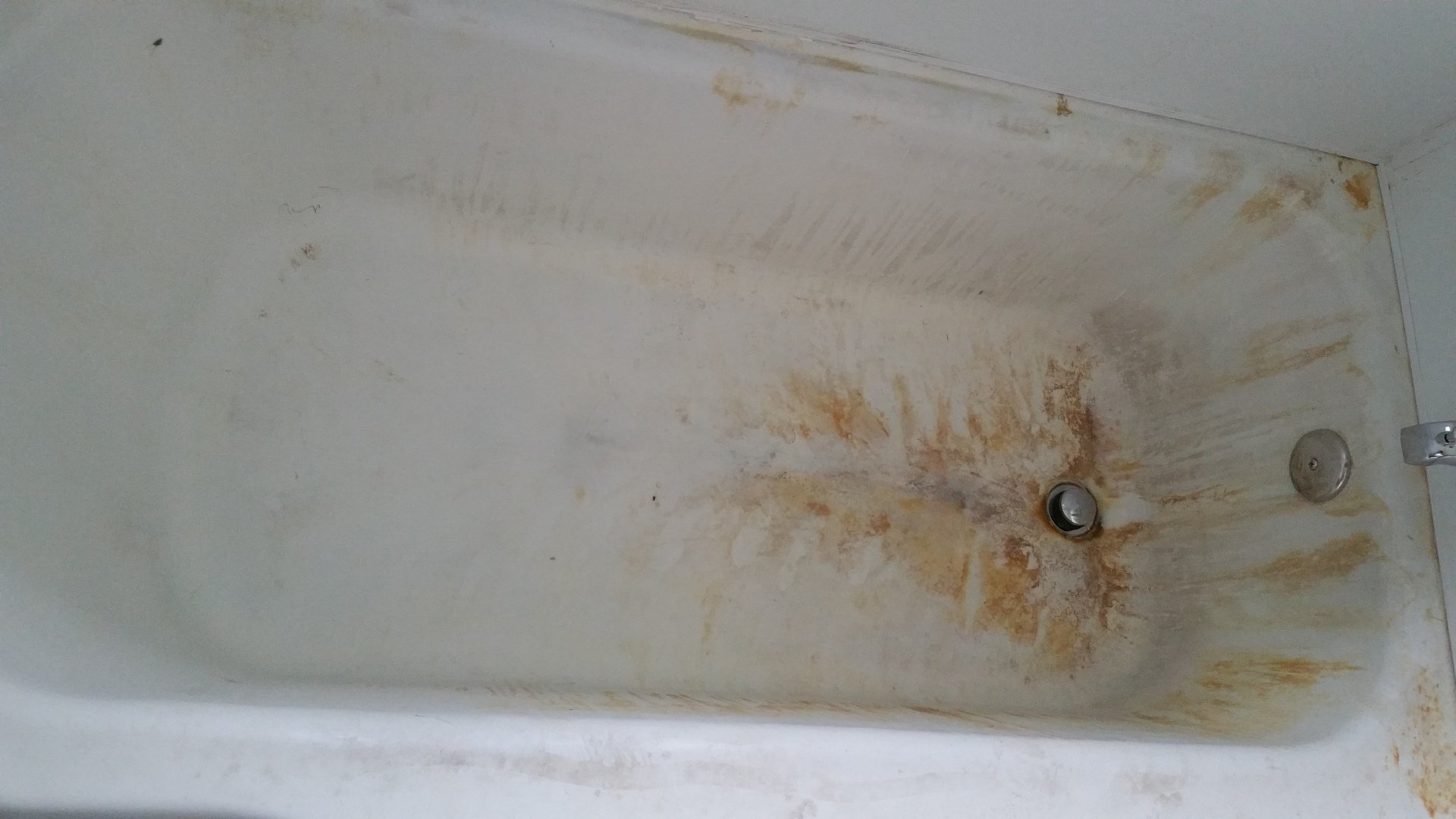 A dirty bathtub in a bathroom with a drain.