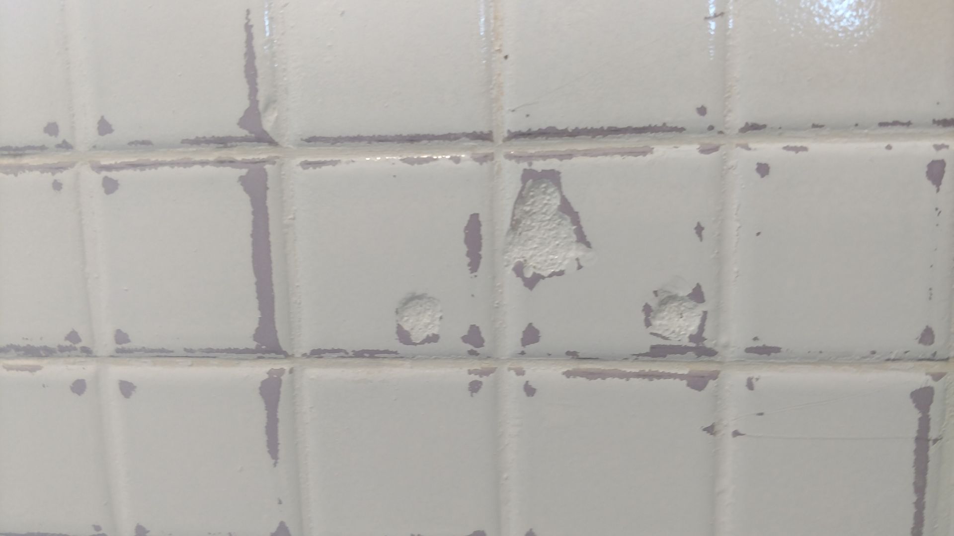 A close up of a white tile wall with peeling paint.