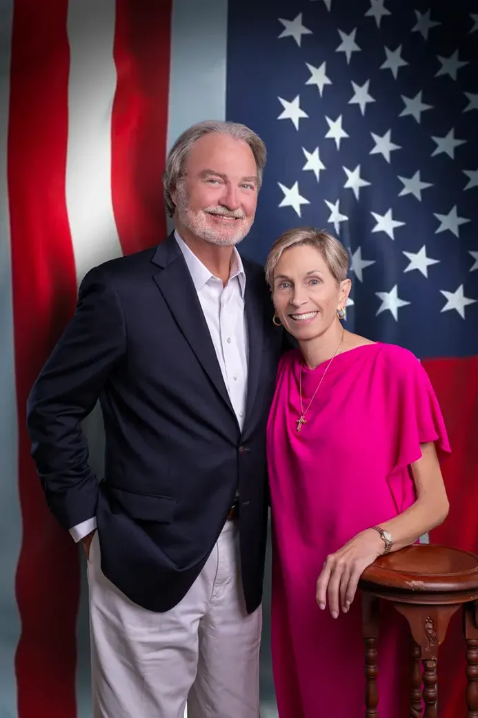 A man and a woman are posing for a picture in front of an american flag.