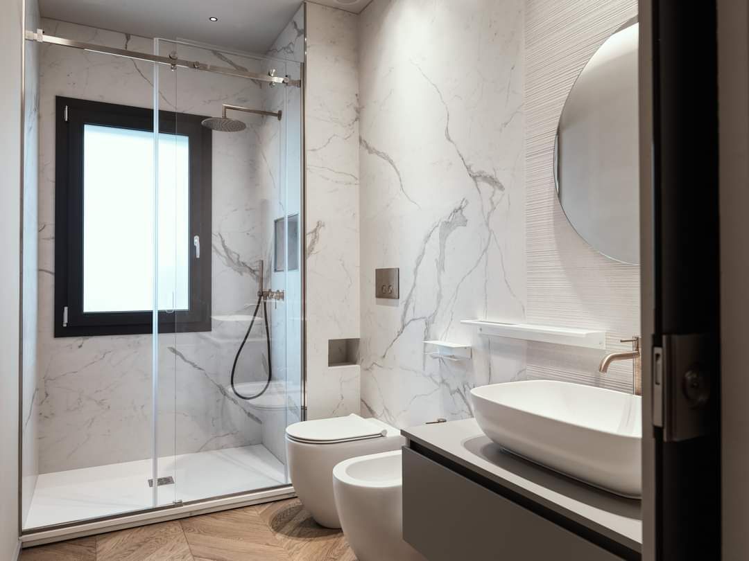 Bagno moderno con doccia in vetro, pareti in marmo, lavabo a parete e bidet-WC.