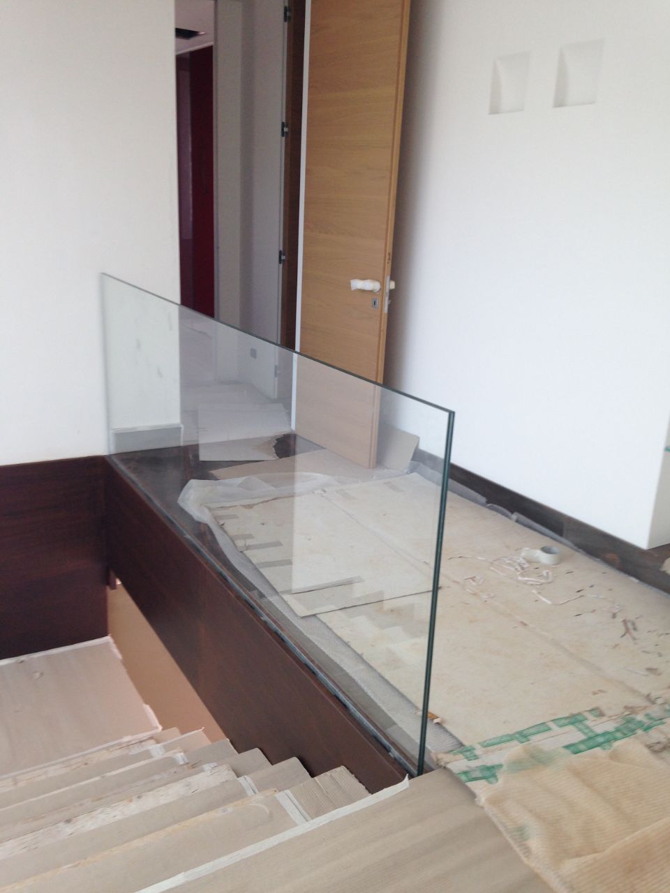 Vano scale interno con ringhiera in vetro e pavimento non rifinito vicino a una porta.
