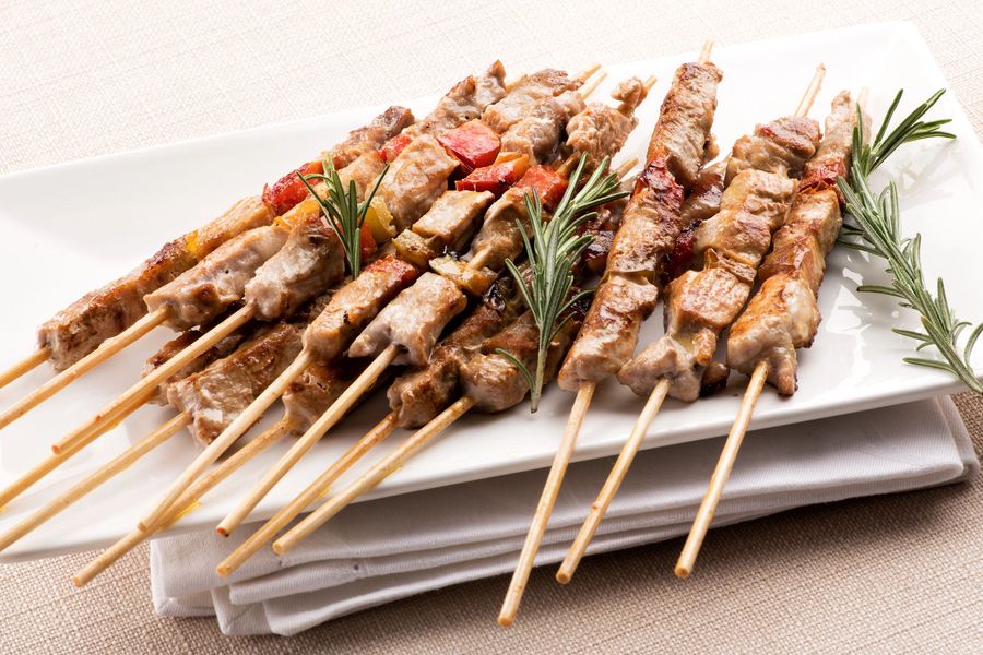 Spiedini di carne e verdure grigliate su un piatto rettangolare bianco.