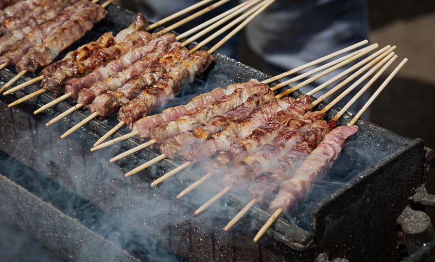 Spiedini di carne cotti sulla brace ardente, con il fumo che sale.