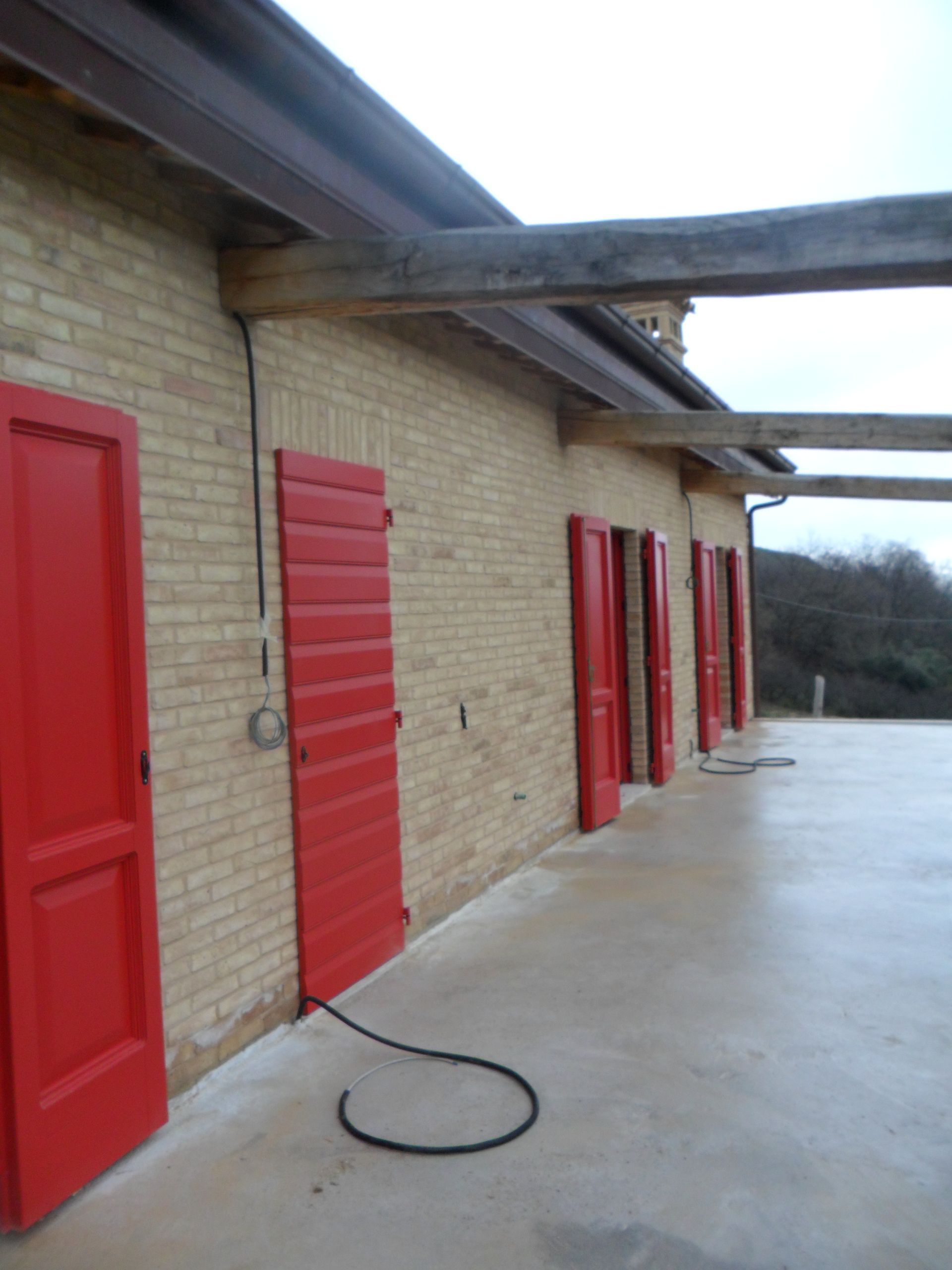 Una fila di porte rosso acceso su un edificio in mattoni color sabbia, con travi in legno che si estendono su un patio in cemento.