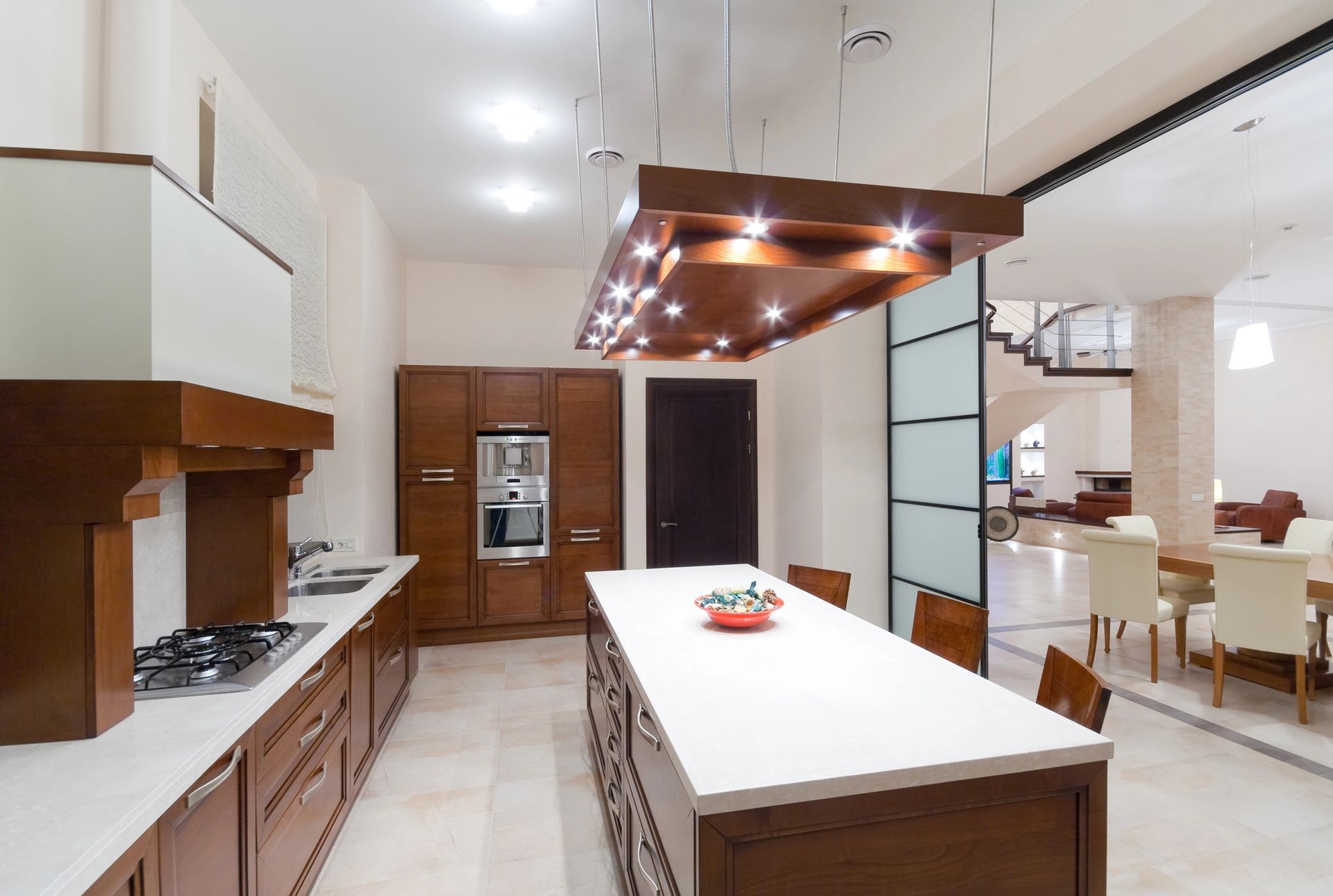 Cucina moderna con mobili in legno, isola centrale bianca, lampadario a sospensione e vista aperta sulla zona pranzo.