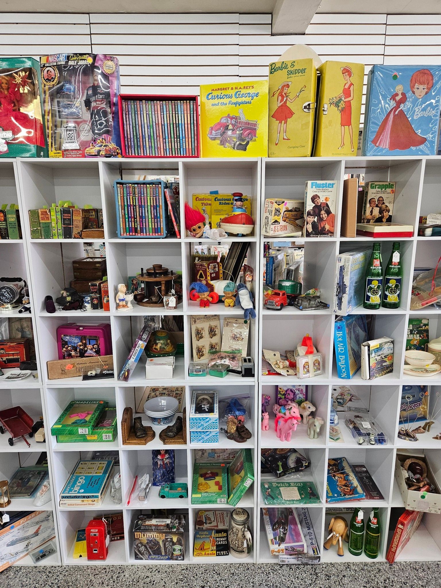 Wall of white cubbies filled with colorful toy and collectible figures, with boxed toys on the top shelves.