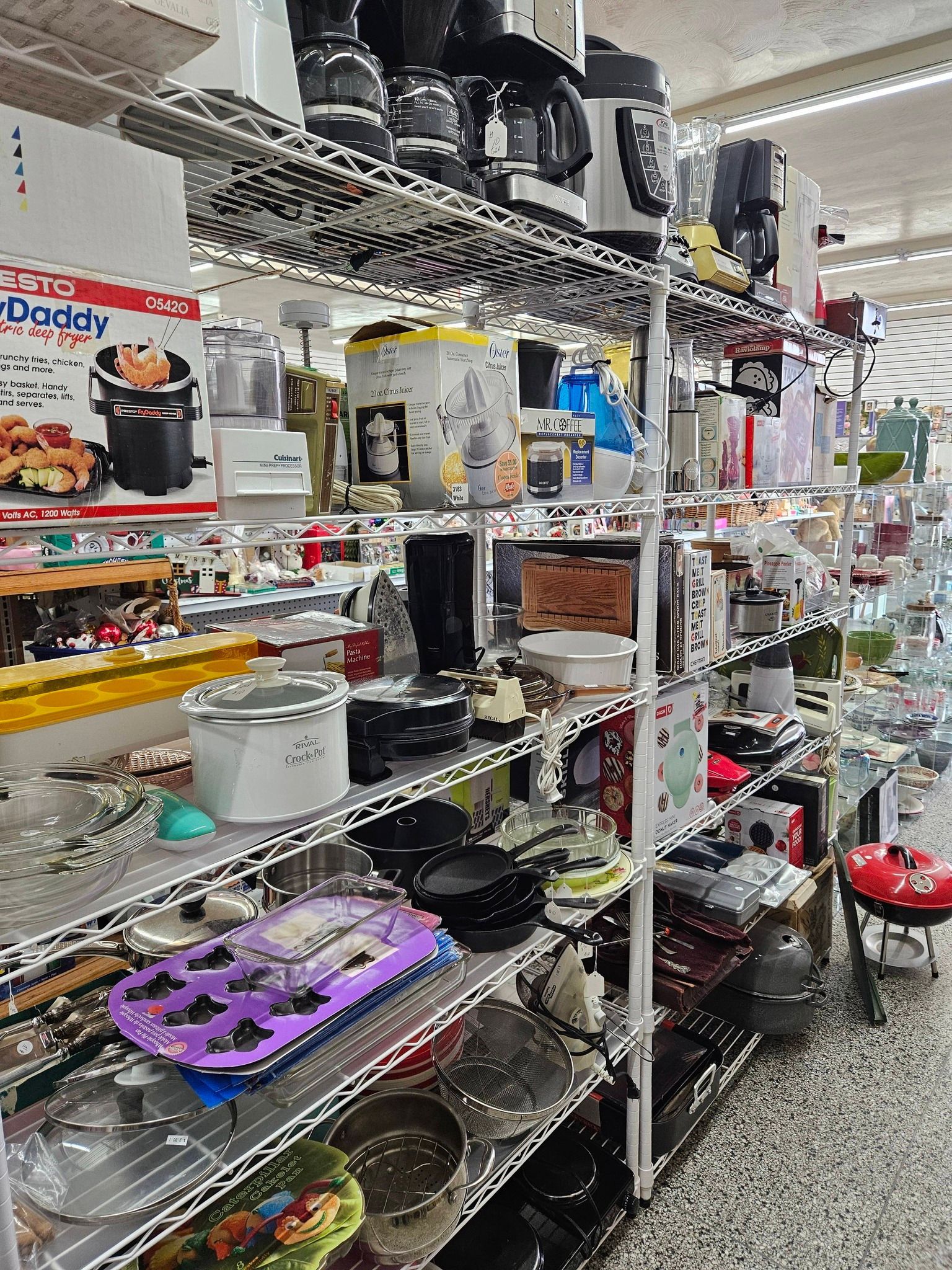 Kitchenware displayed on metal shelves in a store aisle, with pots, pans, and utensils visible.