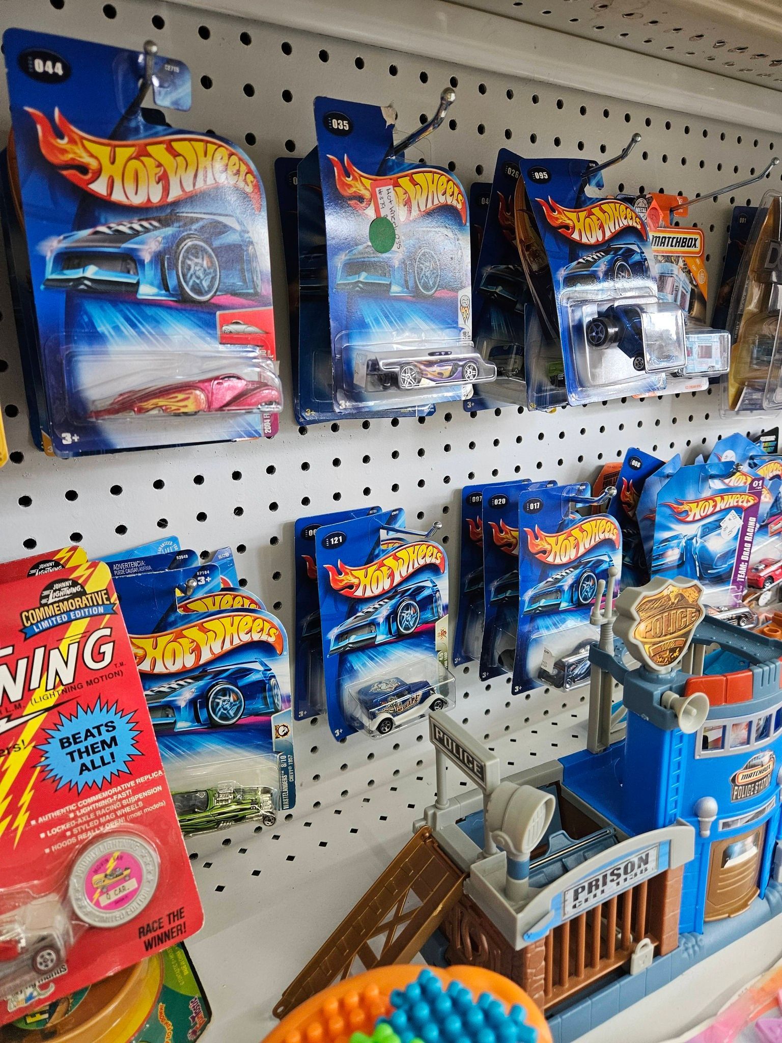 Hot Wheels toy cars and sets displayed on a pegboard shelf in a store aisle