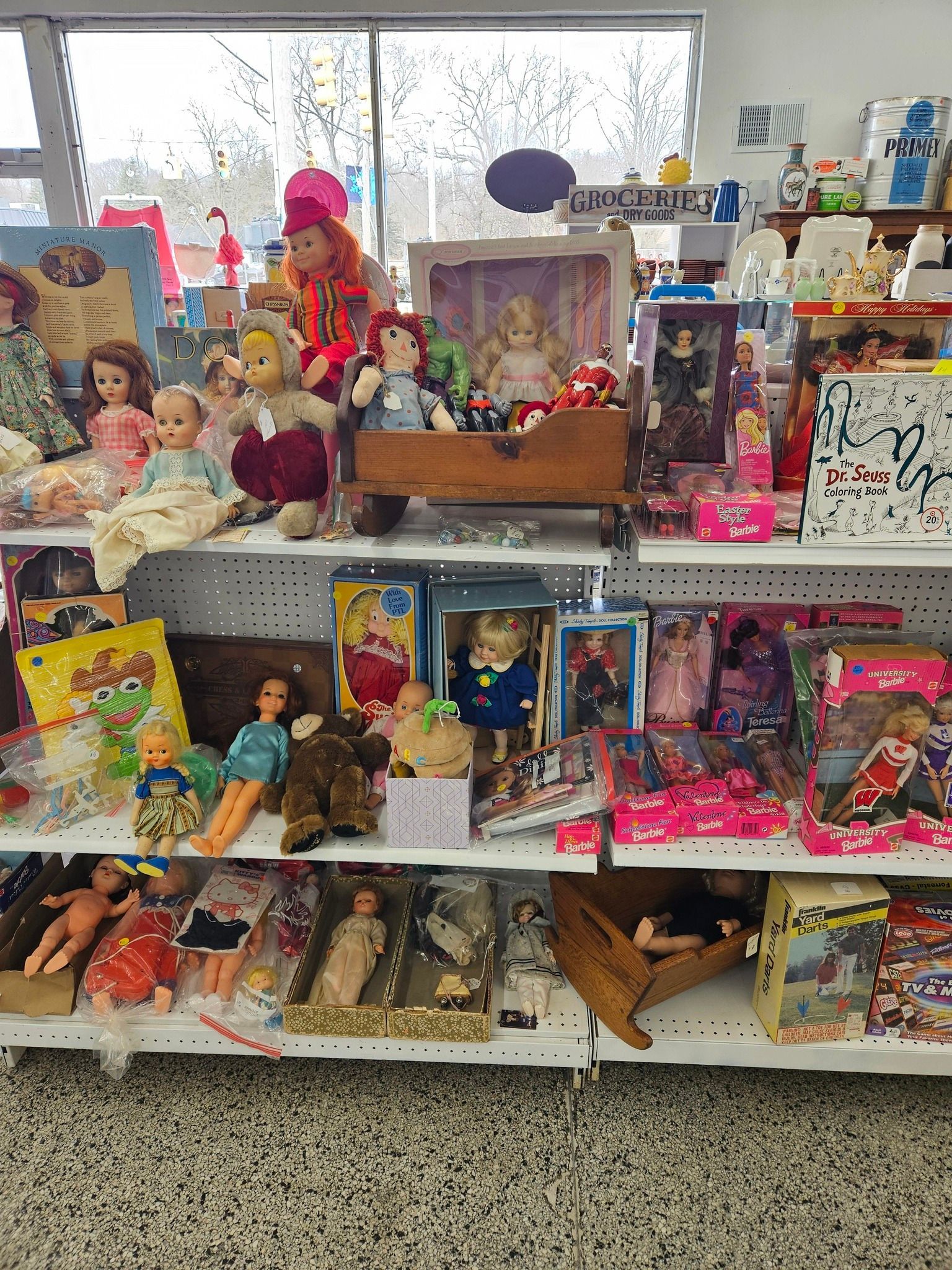 Shelf of assorted dolls and toys arranged in a shop display, with colorful boxes and figures.