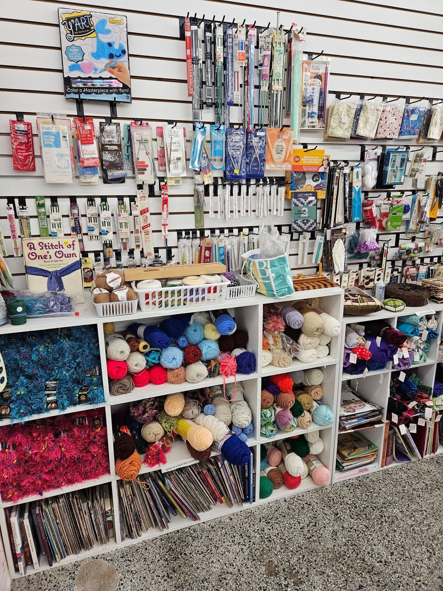 Craft store display with colorful yarn, craft supplies, and accessories arranged on shelves and pegboard.