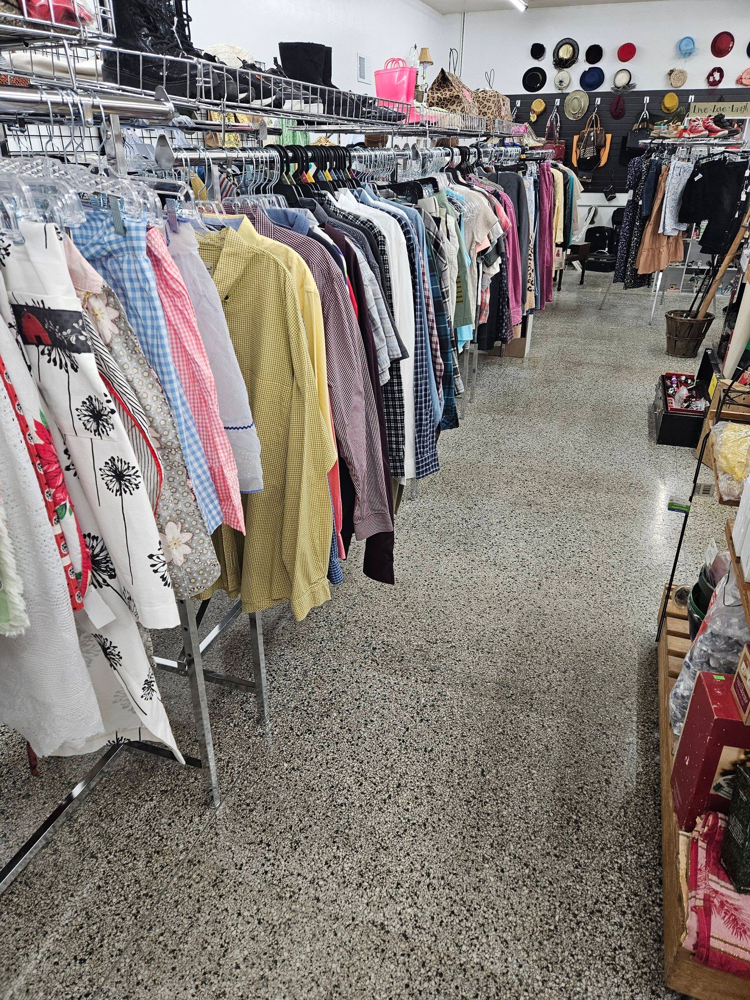 Clothing racks in a thrift store aisle with assorted colorful garments hanging on display.