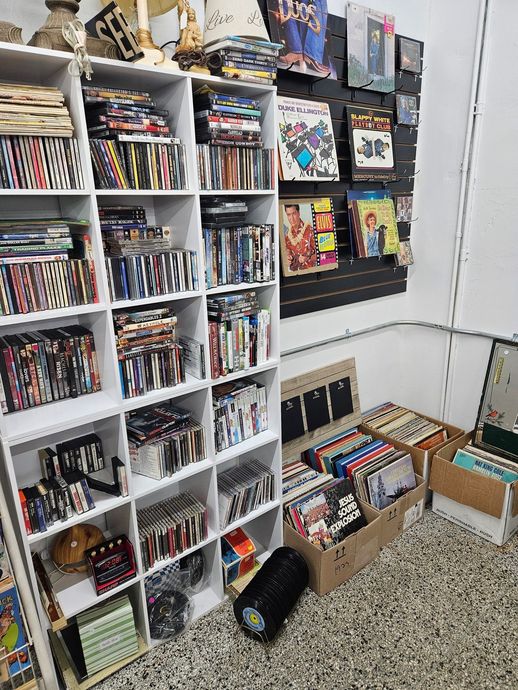 White shelving filled with manga and books, with storage bins and boxes in a room corner