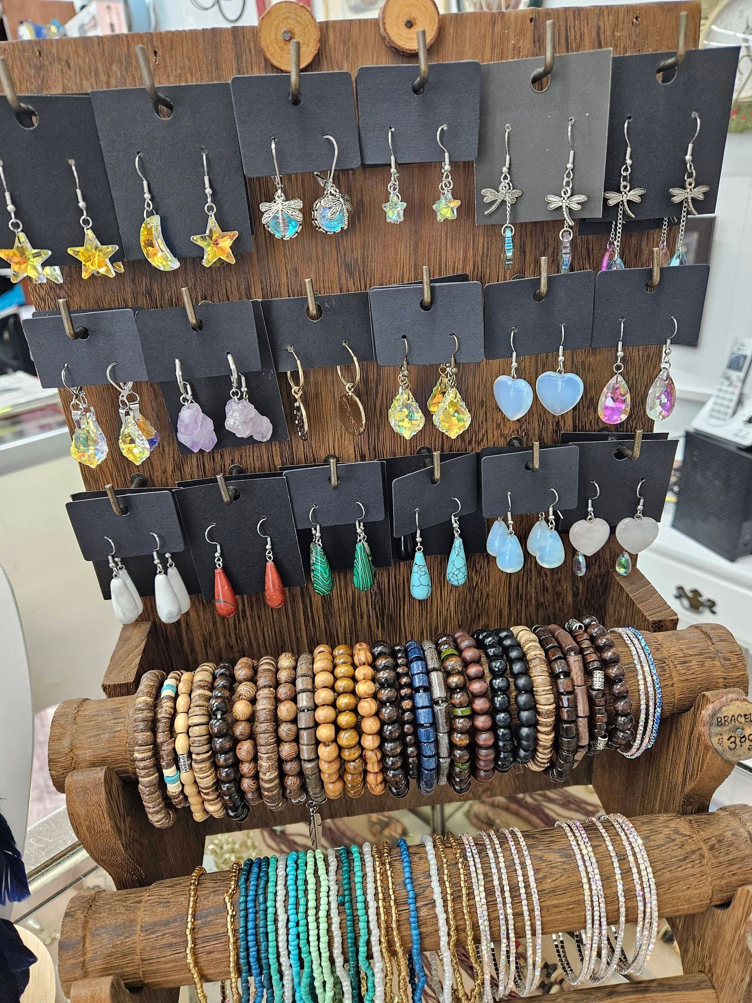 Display of colorful handmade earrings and beaded bracelets on wooden racks at a craft market booth